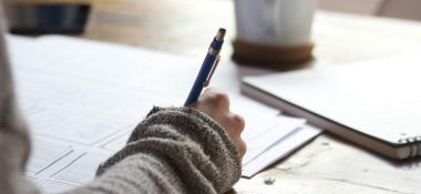 Person holding a pen studies papers spread out on a desk