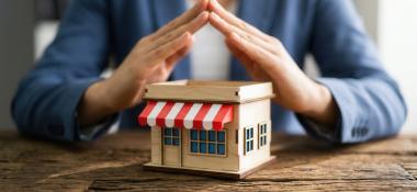 Concept of small business insurance and commercial coverage with a miniature shop model sheltered by hands.
